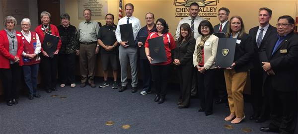 14 adults, some holding proclamation certficates, stand in front of the school board dais